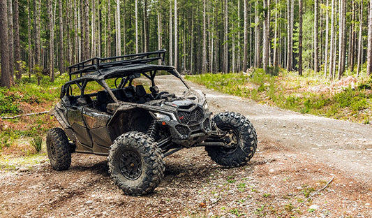 A Can-Am Maverick X3 navigating a dirt road through a wooded area, showcasing its utility terrain vehicle capabilities.