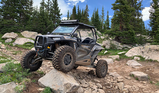 A Polaris RZR 900 navigating rocky terrain in the mountains, showcasing its UTV windshield and protective features.