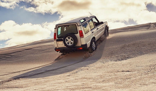 A white SUV navigates a sandy hill, showcasing its off-road capabilities and suitability for UTV accessories and hunting.