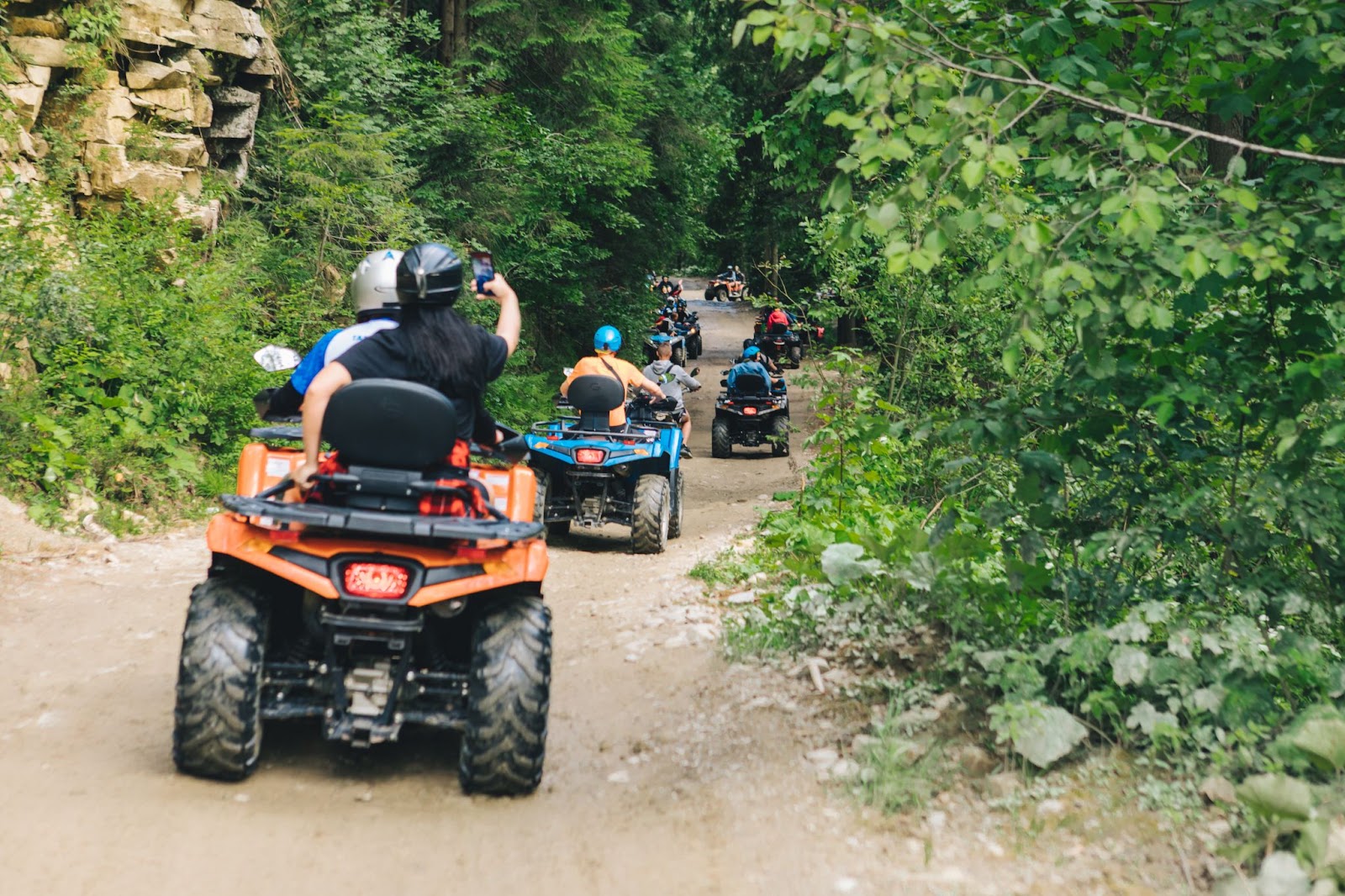 Group of adventurers riding ATVs along a rugged forest trail.