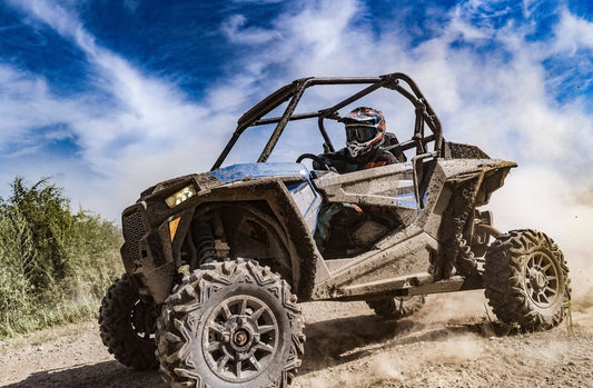 Off-road vehicle with a driver kicking up dust on a trail.