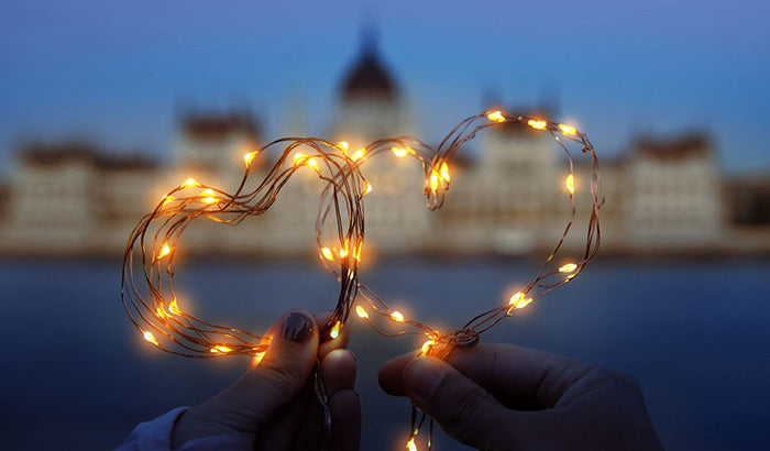 Two hands gently hold a heart-shaped light string, symbolizing love and connection for Valentine's Day celebrations.