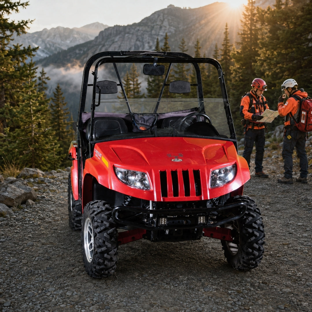 Two riders beside a red Arctic Cat Prowler with half windshield on a gravel road at sunset