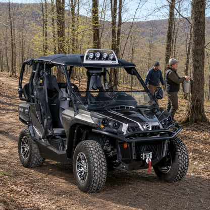 Camo Can-Am Commander with hard top and tilting windshield tilted open on a wooded trail with people alongside. gallery-1
