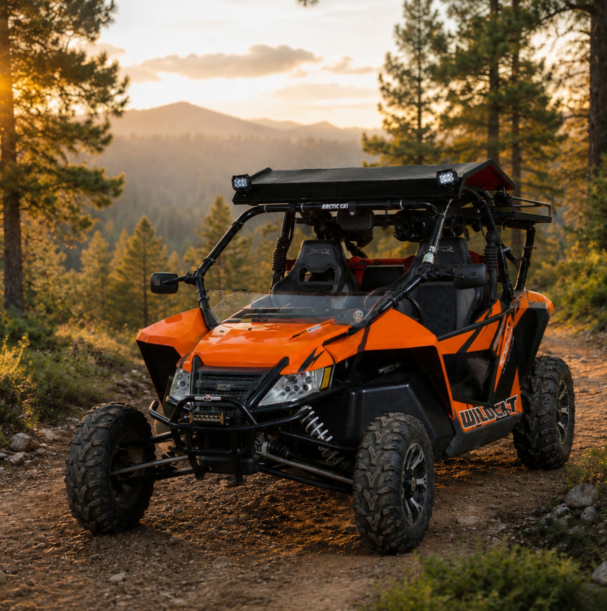 Orange Arctic Cat Wildcat with full windshield on a mountain trail at sunset