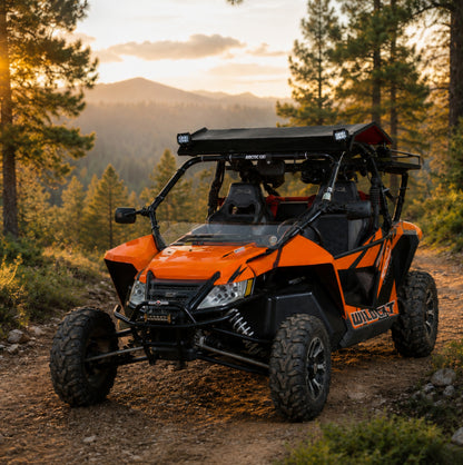 Orange Arctic Cat Wildcat with full windshield on a mountain trail at sunset