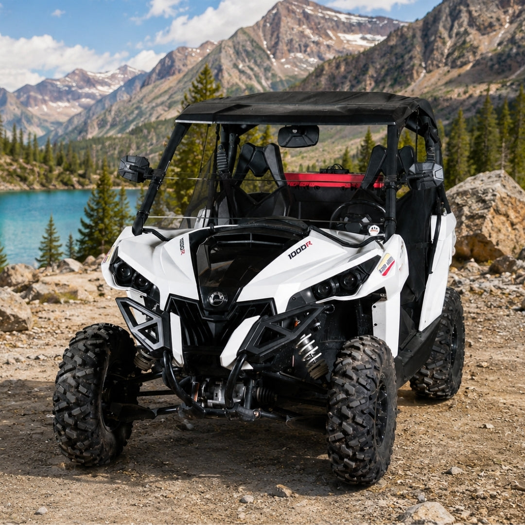 Can-Am Maverick with half windshield parked above an alpine lake ringed by snow-streaked peaks