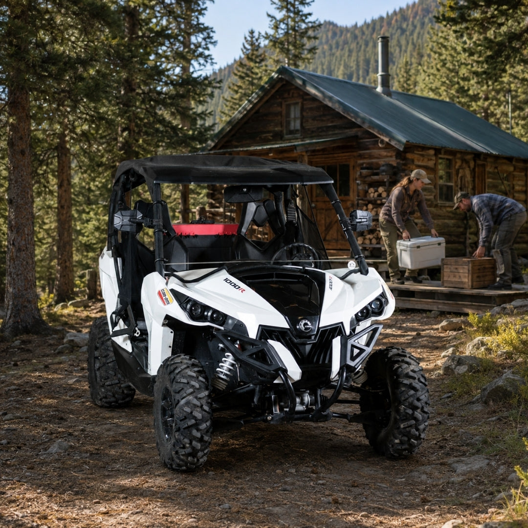 White Can-Am Maverick with full windshield parked by a wooden cabin in the woods