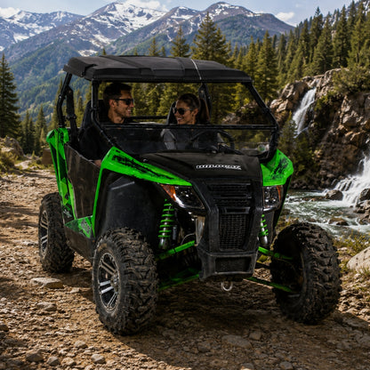 Two riders in a green Arctic Cat Wildcat Trail with hard top and tilting windshield on a rocky mountain trail