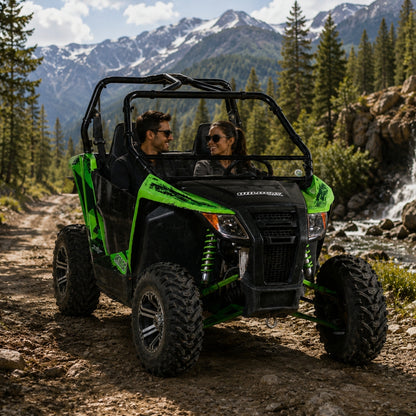 Two riders in a green Arctic Cat Wildcat Trail with no top and tilting windshield on a mountain trail