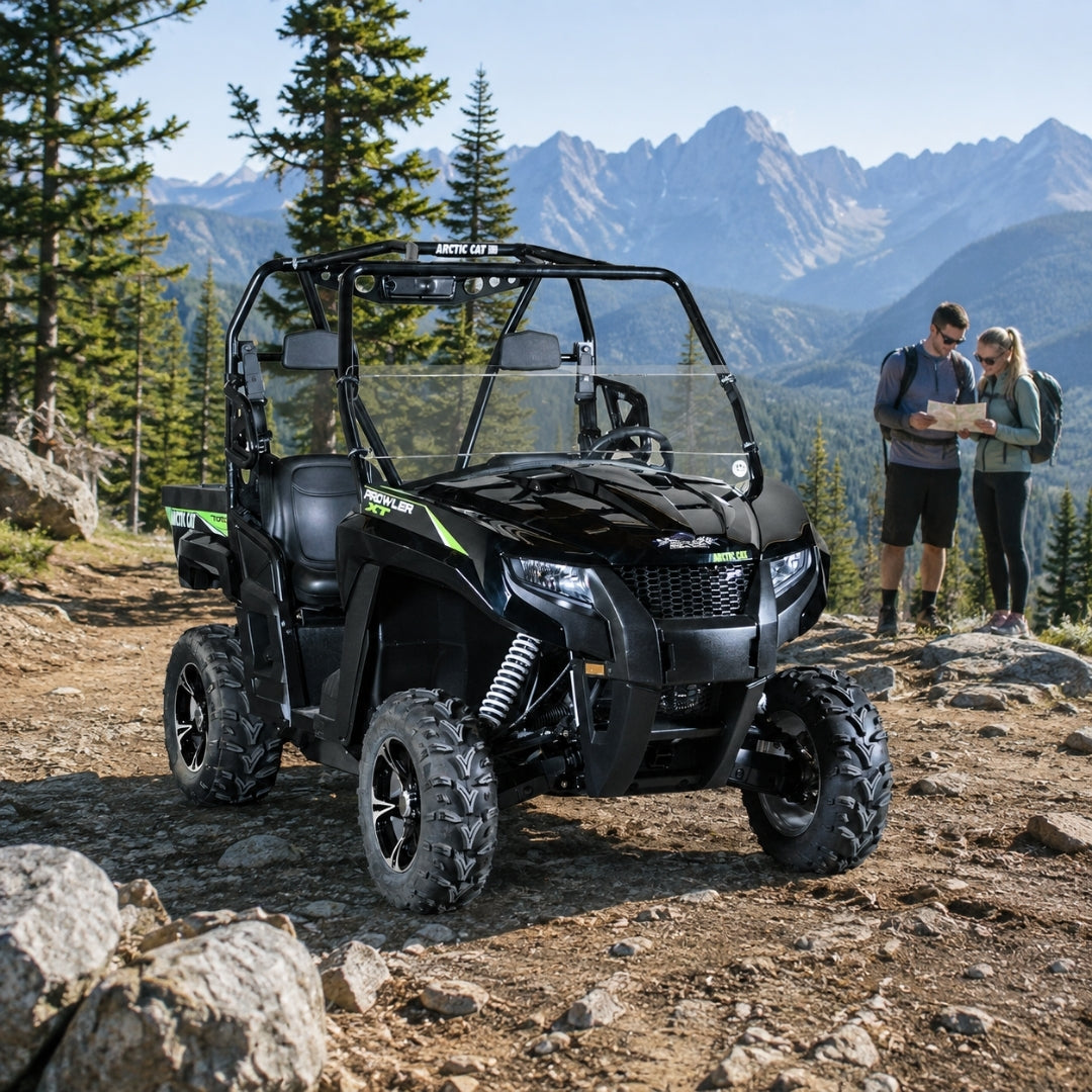 Two people beside a black Arctic Cat Prowler with half windshield on a rocky mountain trail