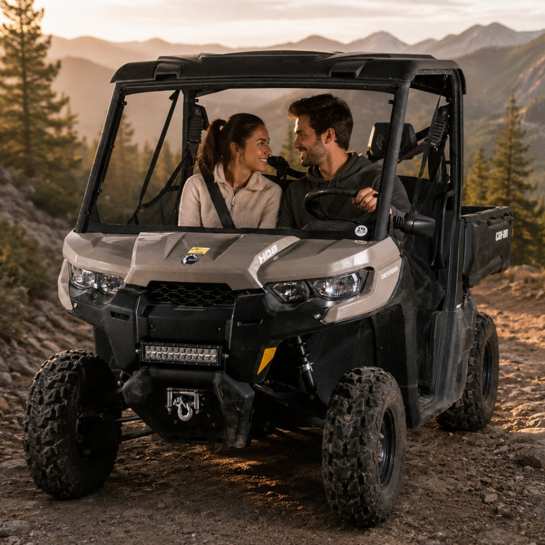 Two riders in a tan Can-Am Defender with full windshield on a mountain trail