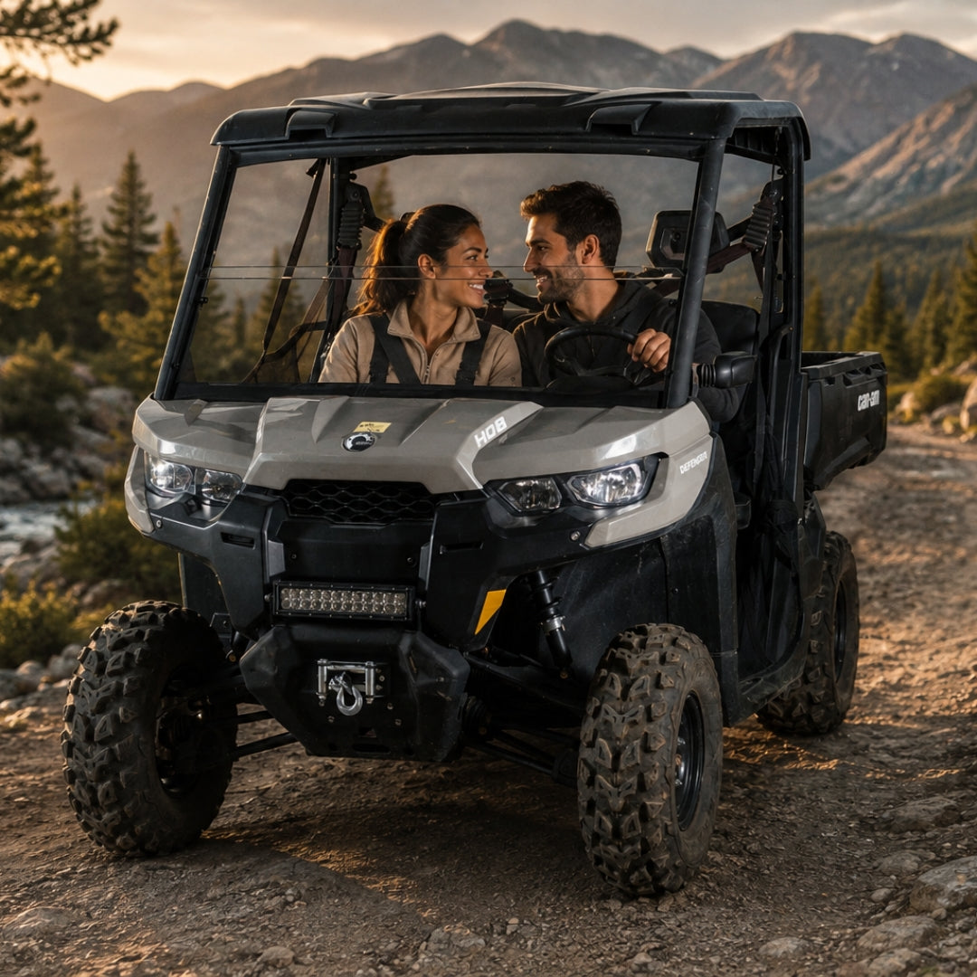 Two riders in a tan Can-Am Defender with half windshield on a mountain trail