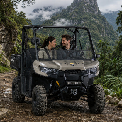 Two riders in a tan Can-Am Defender with tilting windshield on a mountain trail