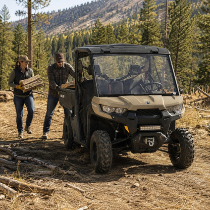 Two people beside a tan Can-Am Defender with full windshield on a wooded trail