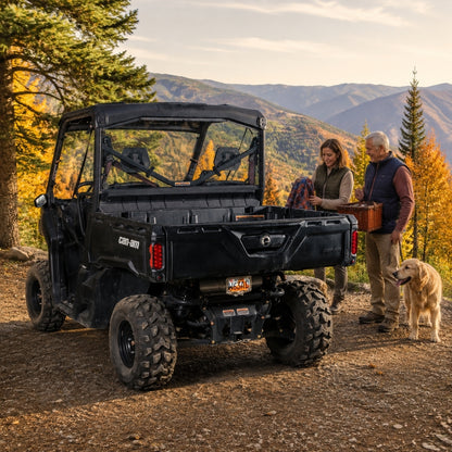 Two people beside a black Can-Am Defender with back windshield on a mountain overlook