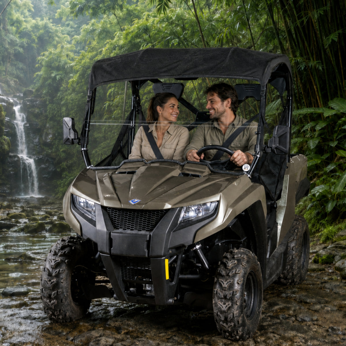 Two riders in a gray Arctic Cat Prowler 500 with half windshield beside a waterfall