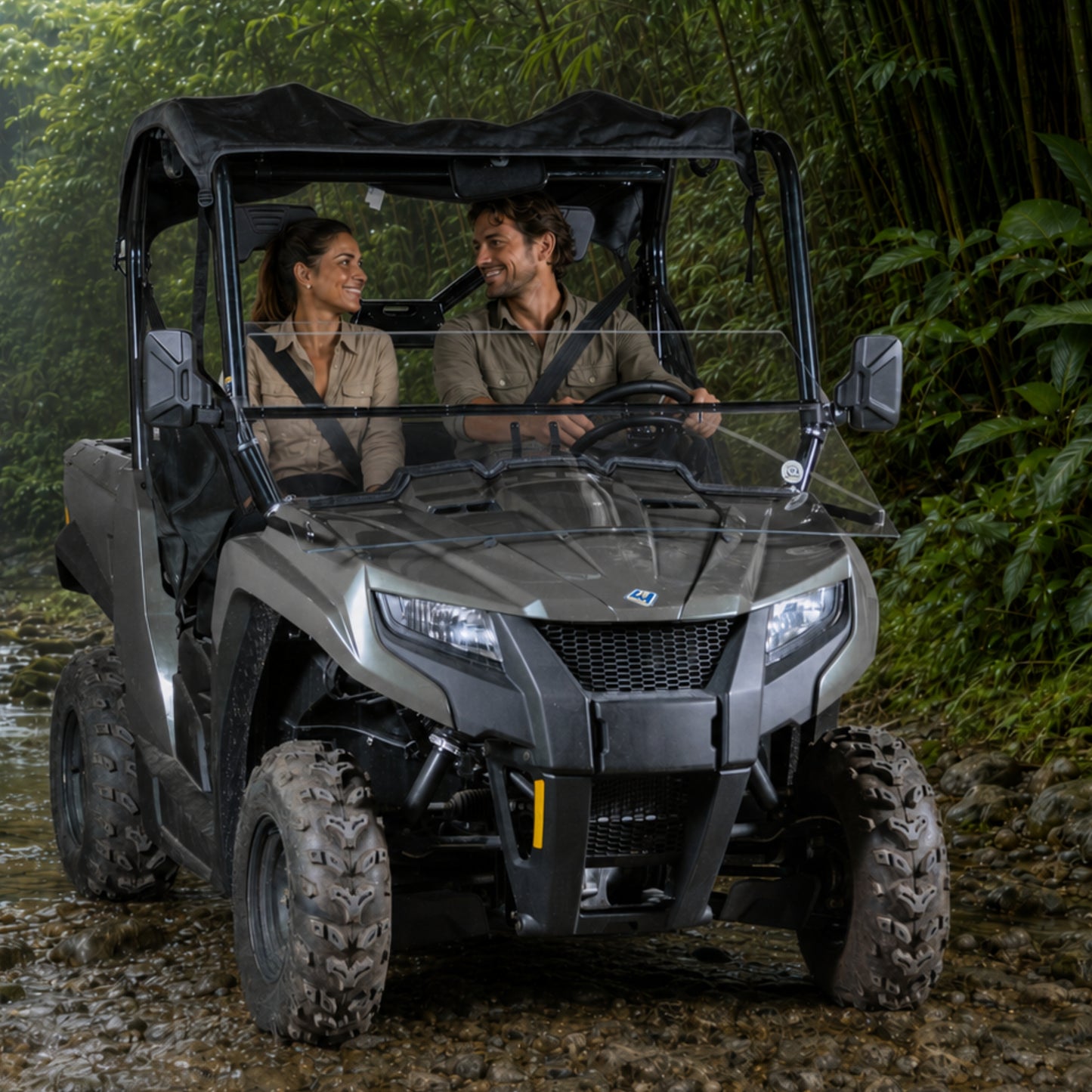 Two riders in a gray Arctic Cat Prowler 500 with tilting windshield on a wooded trail