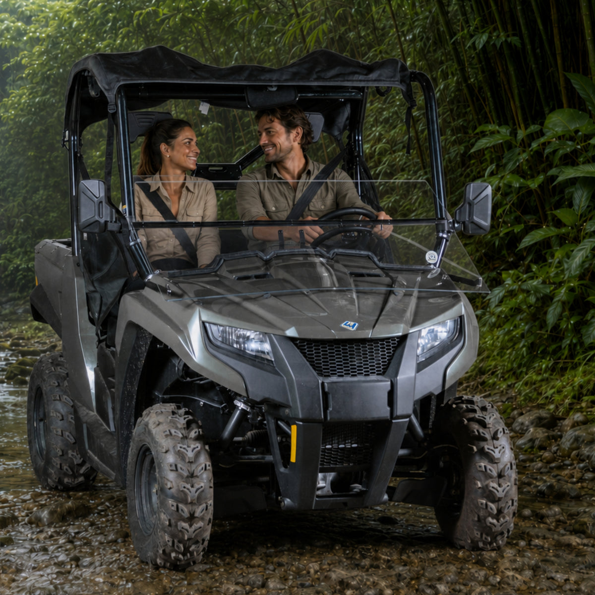 Two riders in a gray Arctic Cat Prowler 500 with tilting windshield on a wooded trail