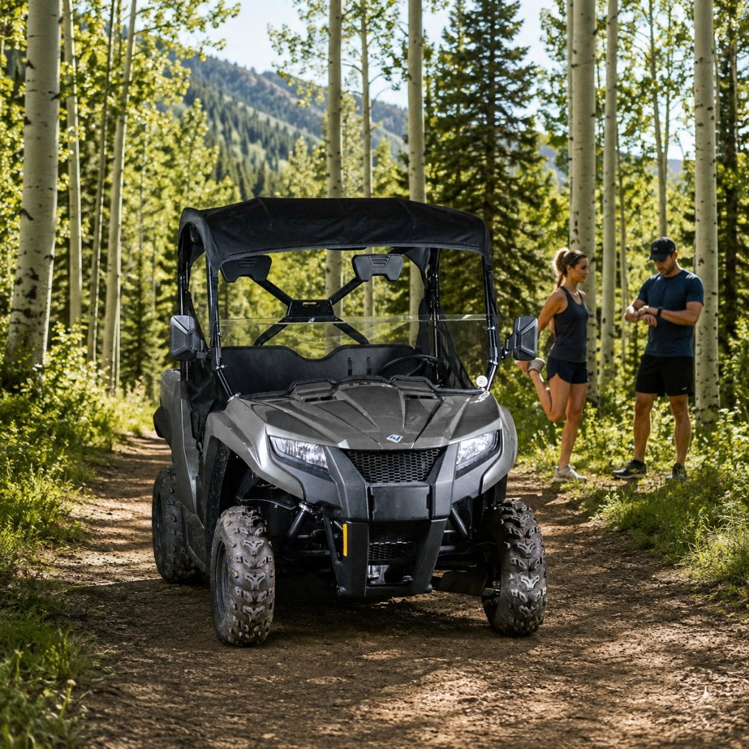 Gray Arctic Cat Prowler 500 with half windshield on a forest trail with a rider standing alongside