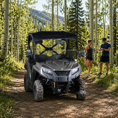 Gray Arctic Cat Prowler 500 with half windshield on a forest trail with a rider standing alongside