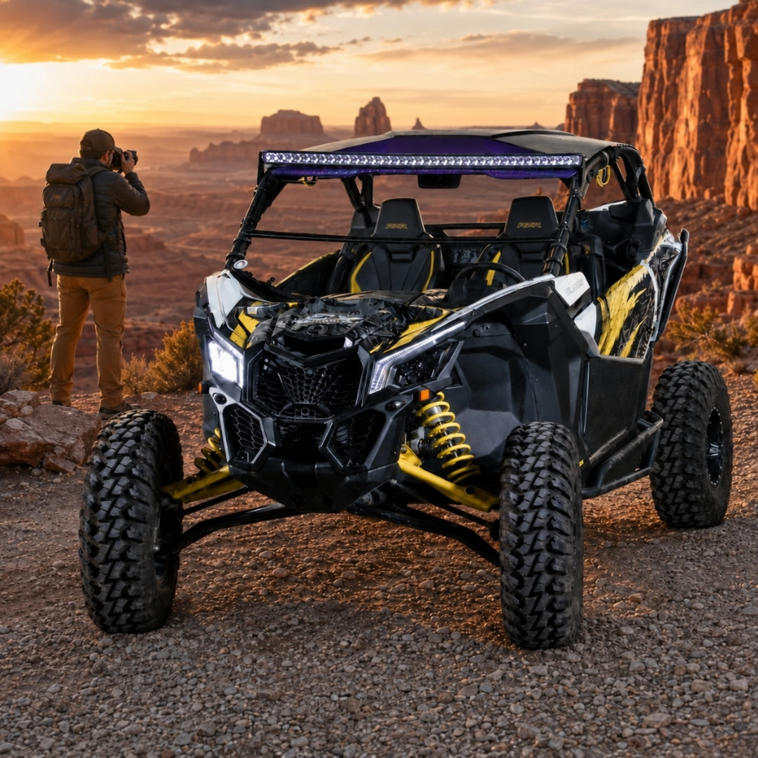 Black and yellow Maverick X3 with tilting windshield on a golden hillside track, person in background. gallery-1