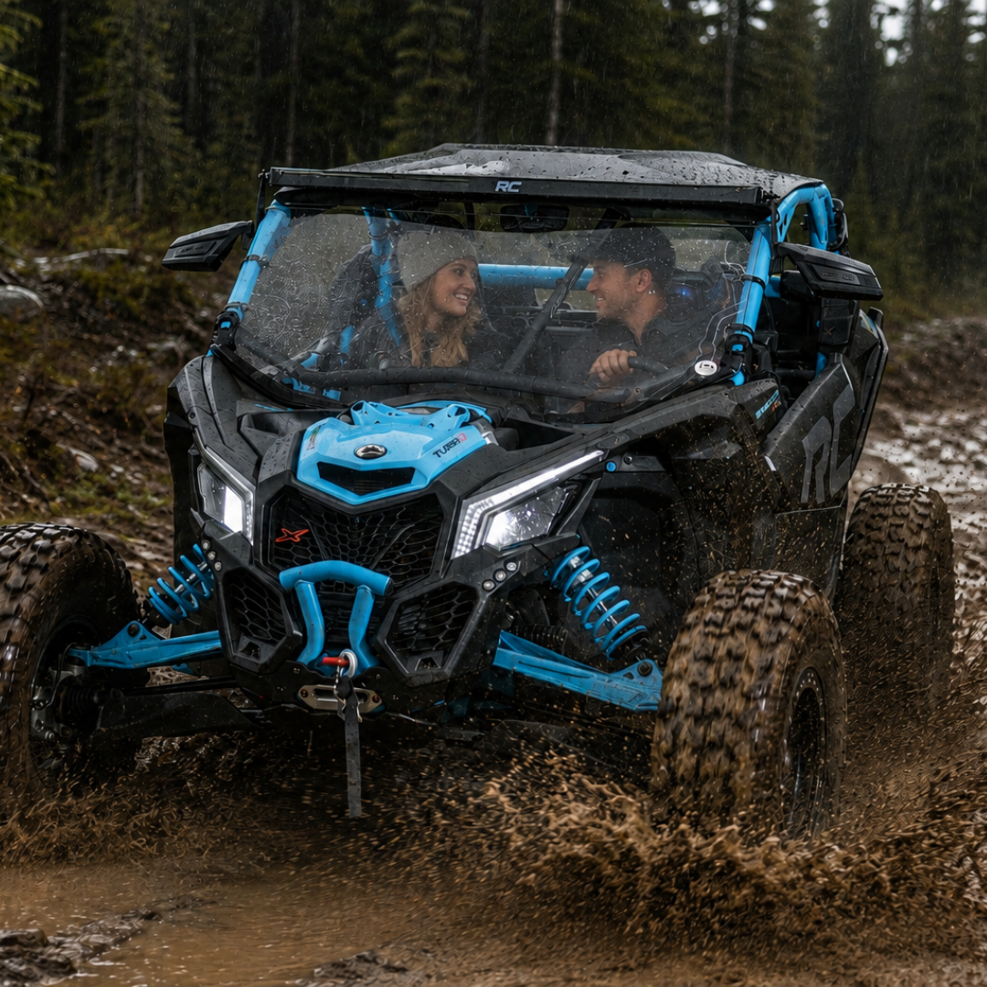 Two riders in a blue Maverick X3 with full windshield on a wooded trail. gallery-1