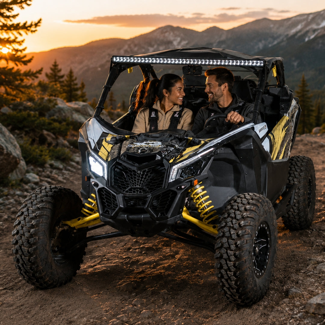 Two riders in a black and yellow Maverick X3 with full windshield on a ridge trail at sunset. gallery-1
