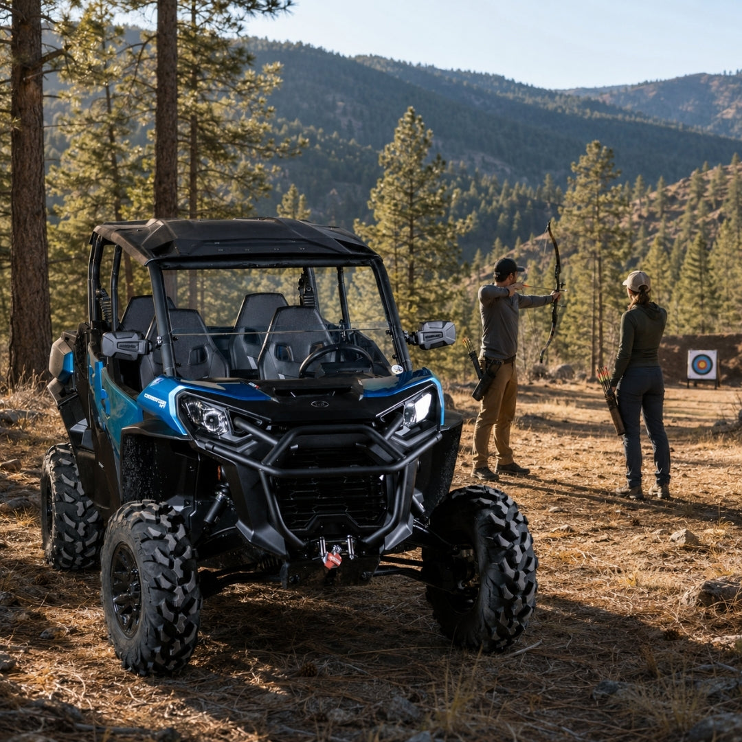 Blue Can-Am Commander with half windshield on a forest trail with people alongside