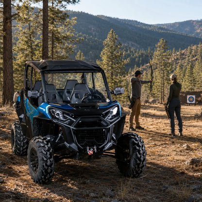 Blue Can-Am Commander with half windshield on a forest trail with people alongside