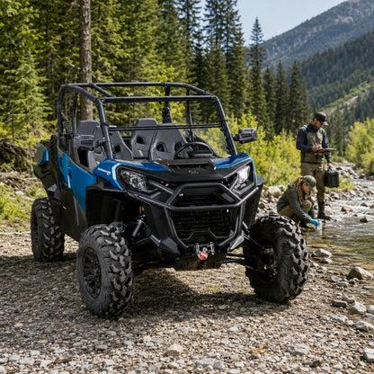 Blue Can-Am Commander with tilting windshield on a forest trail with a person alongside. gallery-2